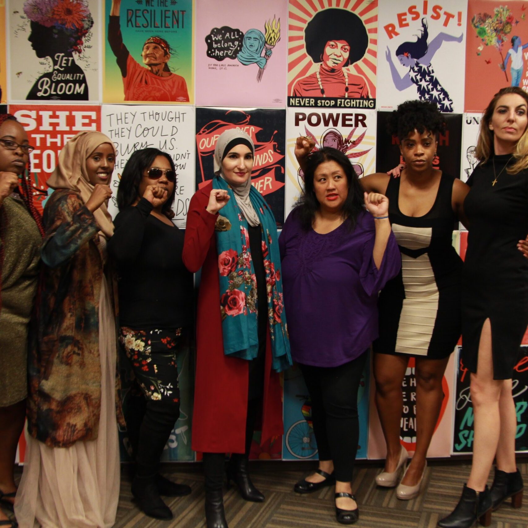 Women of color posing together in front of assorted women's empowerment posters